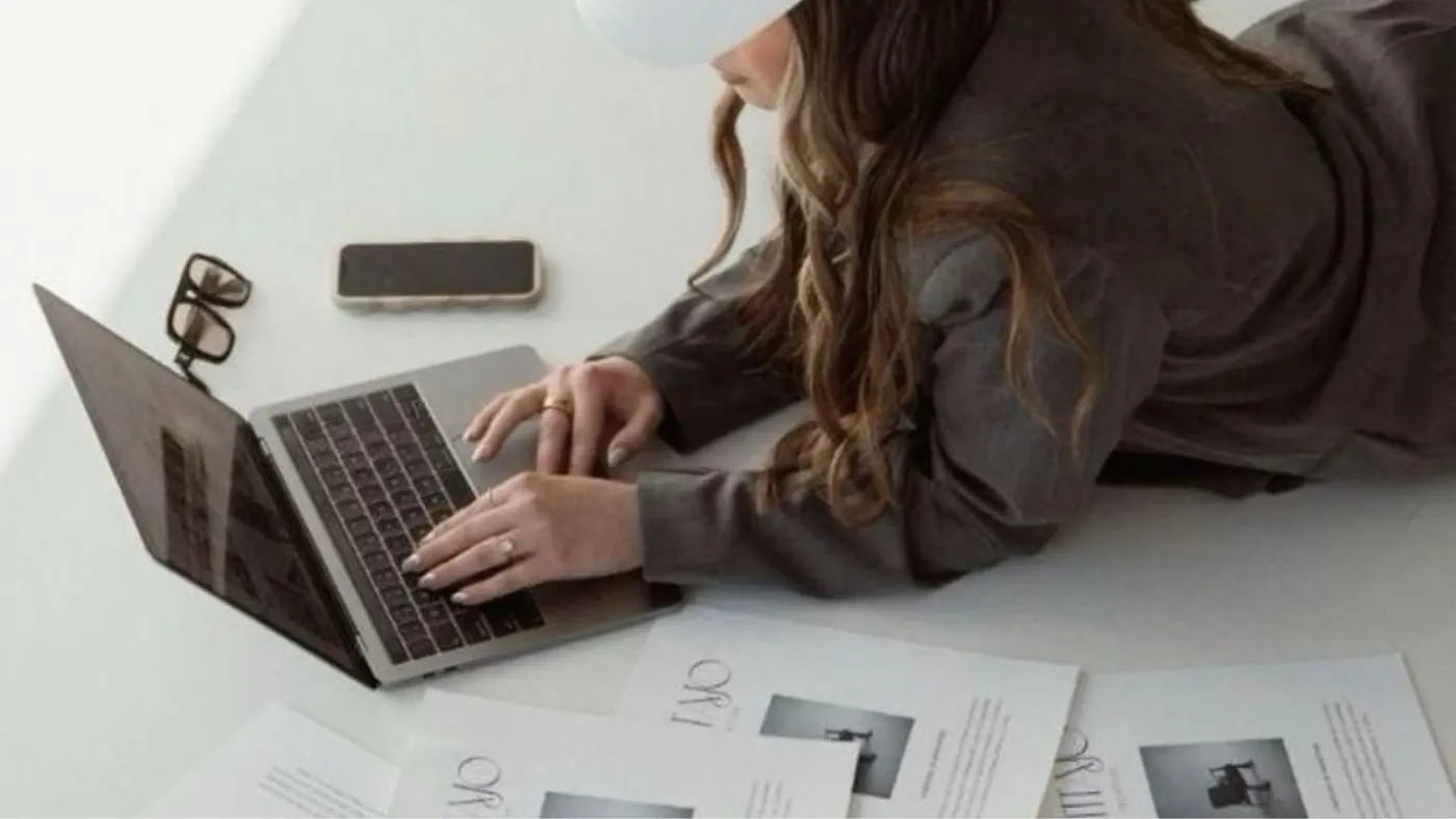 Manos trabajando en un portátil junto a documentos de proyecto